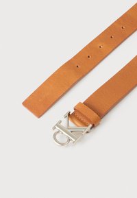 Ταμπά δερμάτινη ζώνη με ασημένια αγκράφα με διαπλεκόμενα γράμματα "CK" και πολλαπλές οπές ρύθμισης σε λευκό φόντο.