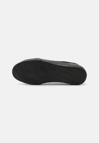 Semelle de basket noire avec caoutchouc texturé, motifs circulaires et rainures pour l'adhérence. Les accents latéraux présentent des détails de couleur subtils.
