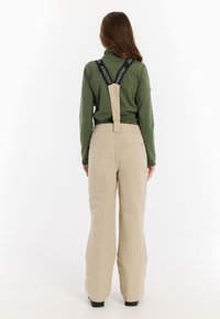 Beige sneeuwbroeken met verstelbare zwarte bretels, met een gladde textuur en een losse pasvorm. De achterkant heeft een eenvoudig ontwerp en minimale branding.