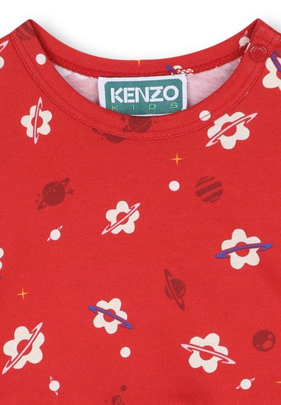 T-shirt en coton rouge présentant un motif de fleurs blanches et de planètes de différentes couleurs, avec un col rond et une étiquette cousue.