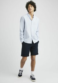 Chemise à rayures bleu clair et blanche, shorts navy et baskets noires. Manches courtes et poches sur les shorts, coupe décontractée.