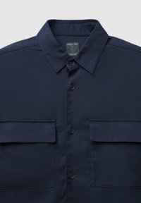 Camicia blu navy realizzata in tessuto intrecciato, con colletto classico, chiusura frontale con bottoni e due tasche sul petto con pattine.
