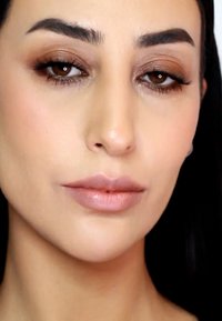 Gros plan sur un visage avec une peau lisse et claire, des lèvres roses douces, un fard à paupières brun subtil, des sourcils bien définis et des cheveux raides et foncés.