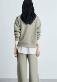 Lichtgroene sweatshirt met een relaxte pasvorm, geribde mouwen, gedragen over een witte shirt, gecombineerd met bijpassende wijde broek. Zachte textuur.