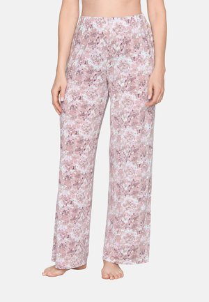 Woman wearing loose, wide-leg pants with a pink and white floral pattern, standing barefoot against a plain background.