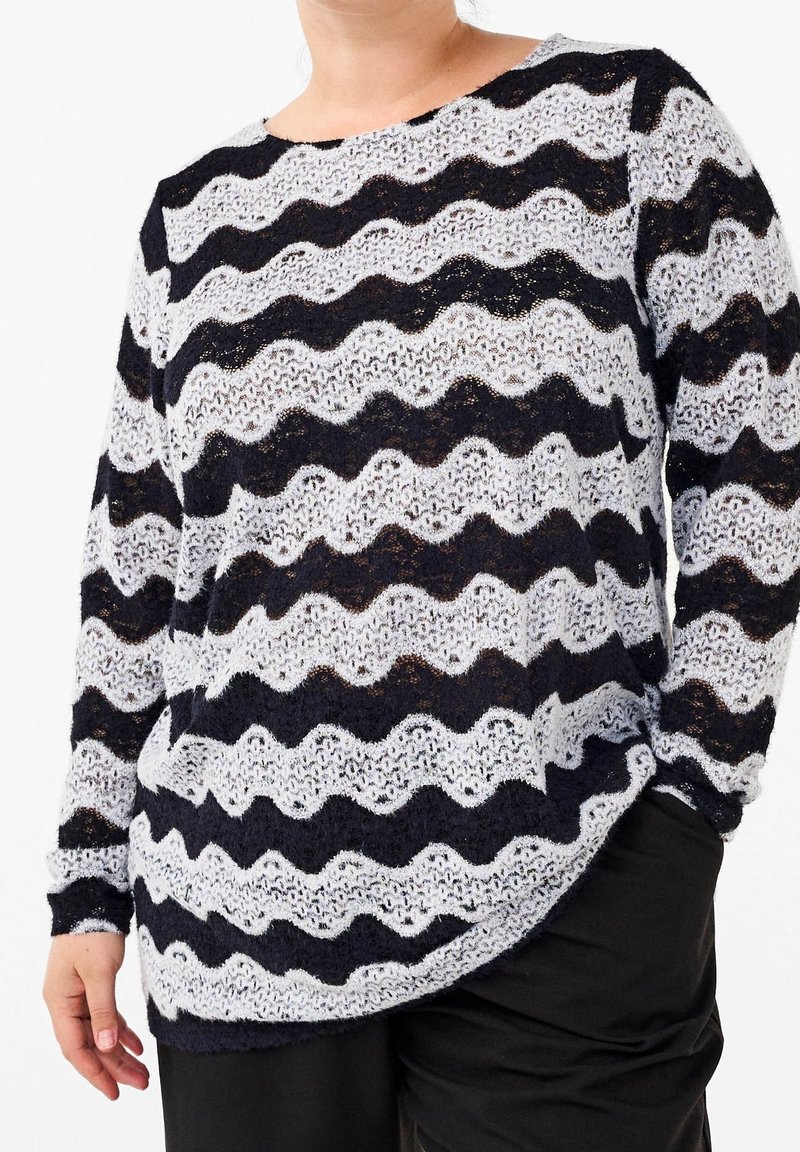 Sweter z dzianiny koronkowej w faliste czarno-białe paski. Okrągły dekolt i długie rękawy. Tkanina ma strukturalny, otwarty splot.