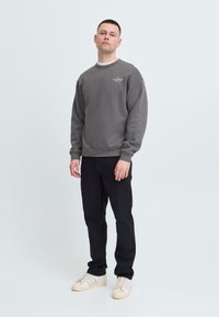 Grå hettegenser med ribbestrikkede mansjetter og halslinning, sammen med svarte bukser og beige joggesko. Uformell passform, enkelt design, minimal merking.