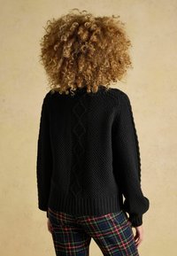 Czarny sweter dzianinowy z teksturowanym wzorem i ściągaczami. Posiada wzór w diamenty wzdłuż szwu pleców. Połączony z spodniami w kratę.