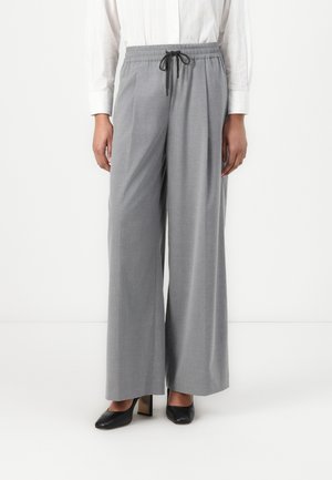 Woman wearing light grey wide-leg trousers with black drawstring, white long-sleeve shirt, and black heeled shoes, standing against white background.