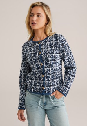 Cardigan bleu marine et blanc à motif avec un col rond, des manches longues et cinq boutons dorés sur le devant. Texture en maille douce.