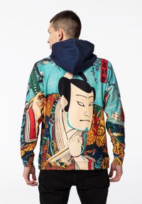 Mnohofarebná mikina s kapucňou, ktorá obsahuje detailný tlač Ukiyo-e. Hlavné farby sú tyrkysová, oranžová a tmavomodrá. Kapucňa kontrastuje s dizajnom.