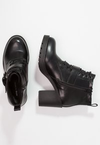 Botines de cuero negro con un chunky block heel, parte delantera con cordones, cremallera lateral y suela de goma texturizada para mayor agarre.