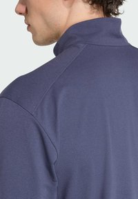 Námornícky modrý dlhý rukáv s vysokým golierom, s hladkou textúrou a prešitým detailom na pleci, zobrazený z bočného pohľadu.