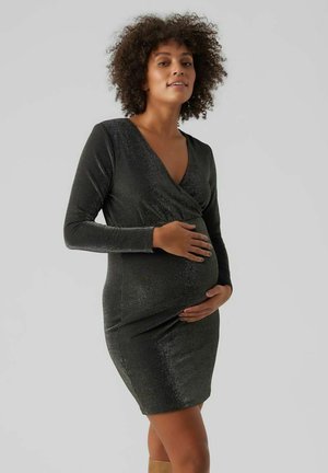 Abito premaman in nero lucido, con scollatura a V e maniche lunghe. La vestibilità aderente esalta la forma naturale. Tessuto morbido e testurizzato.