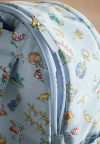 Ljusblå tygryggsäck med olika lekfulla mönster, inklusive djur och föremål, med en gulddragkedja och en mjuk yta.
