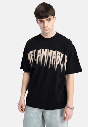 Czarny bawełniany t-shirt o luźnym kroju, krótki rękaw, z napisem "INFLAMMABLE" w białym, spływającym wzorze na klatce piersiowej.