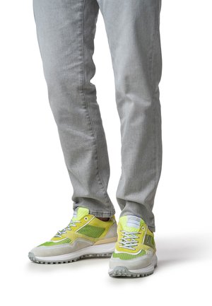 Limettengrüne und graue Sportschuhe mit Mesh-Einsätzen, strukturierten Akzenten und Schnürsenkeln. Getragen mit hellgrauen, schmal geschnittenen Denim-Jeans.