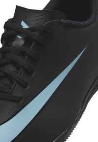 Scarpa sportiva nera con una superficie liscia e testurizzata, dotata di una swoosh azzurra chiara e lacci neri. Suola in gomma progettata per la trazione.