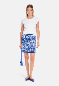 White short-sleeve top, blue patterned skirt with abstract designs, blue handbag, and matching blue flats, featuring a sleek, fitted silhouette.