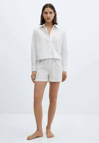 Vitrandig kortärmad skjorta med knäppning och krage, matchande shorts. Lättviktigt tyg, avslappnad passform, subtil textur.