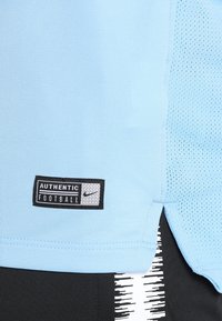 Hellblauses Sportshirt mit Netz-Akzenten, versehen mit einem schwarzen "AUTHENTIC FOOTBALL"-Label und dem Nike-Logo auf der unteren linken Seite.