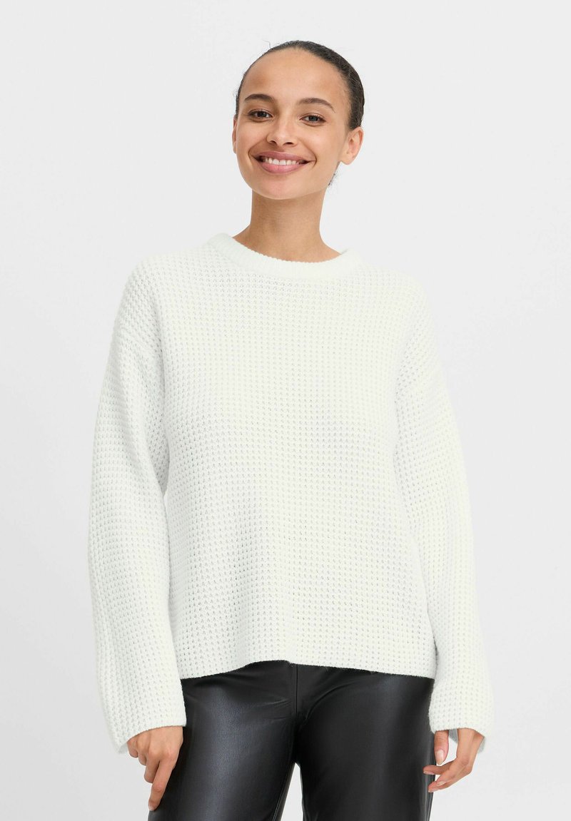 Maglione bianco lavorato a maglia con una vestibilità rilassata, maniche ampia e colletto a coste. Texture liscia, abbinato a pantaloni in pelle nera.