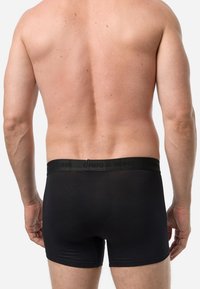Boxer neri con vita elasticizzata morbida, caratterizzati da un branding discreto. Il tessuto appare liscio e aderente.