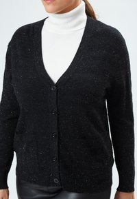 Cardigan nero realizzato in tessuto a maglia testurizzato, con scollo a V, sette bottoni e tasche frontali. Presenta lievi striature bianche all'interno.