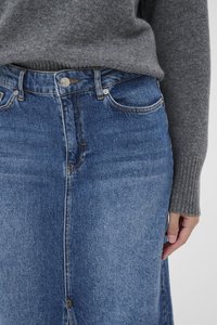 Med-blue denim-hame, jossa on viisi taskua, vetoketjuhalkio ja etuleikkaus. Mukana harmaa neulepaita.