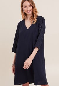 Navy-blaues V-Ausschnitt-Kleid mit dreiviertellangen Ärmeln, das mit strukturierten Spitze-Akzenten an den Ärmeln und einem lässigen Schnitt versehen ist.