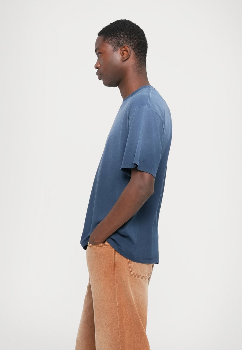 Blaues T-Shirt mit Rundhalsausschnitt aus Baumwolle mit kurzen Ärmeln, locker geschnitten und mit einer leicht strukturierten Oberfläche, kombiniert mit beigen weiten Jeans.