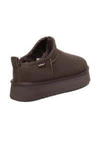 Brauner Slip-On-Hausschuh mit plüschgefüttertem Inneren, dicker Sohle und „EVERAU“-Stoffetikett an der Seite, schräg dargestellt, um Rücken- und Seitenansicht zu zeigen.