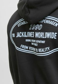 Czarna bluza z kapturem z dużą grafiką w jasnoniebieskim tekście, która zawiera "JACK&JONES WORLDWIDE" oraz datę założenia "1990".