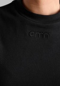 Sort bomulds t-shirt med rund halsudskæring og diskret broderet branding på brystet. Glat tekstur og tætsiddende design.