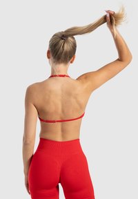 Top deportivo rojo con un diseño simple, tirantes ajustables y cierres metálicos. Combinado con leggings rojos de cintura alta que presentan una textura acanalada.