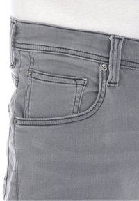 Graue Denim-Jeans mit einer taillierten Passform, die eine Vordertasche und metallische Hardware-Details am Bund und an der Tasche aufweisen.