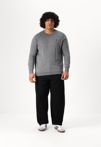 Pulover gri din tricot cu mâneci lungi, asortat cu pantaloni negri largi și adidași albi cu dungi negre. Design simplu, detalii minime.