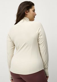 Langarmtop van zacht beige stof met een hoge kraag, voorzien van een getailleerd ontwerp en naaddetails voor een op maat gemaakte pasvorm.