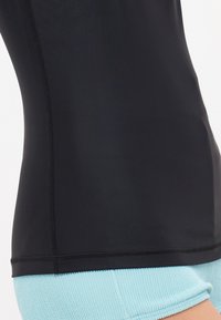 Μαύρο κοντομάνικο τοπ εφαρμοστού σχεδιασμού, φτιαγμένο από λείο ύφασμα. Συνδυασμένο με υφασμένα ανοιχτό μπλε σορτς. Ορατές ραφές στο στρίφωμα.