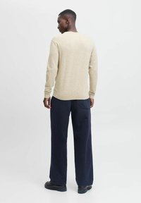 Beige Strickpullover mit langen Ärmeln, Rundhalsausschnitt und schmalen Bündchen. Kombiniert mit weit geschnittenen Hosen in Dunkelblau. Glatte Textur, lässiges Design.