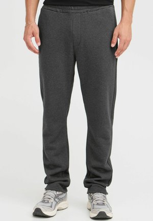 Grå joggebukser laget av myk, strikket stoff. Har elastisk midjebånd, side-lommer, og rette ben. Kombinert med grå sneakers.