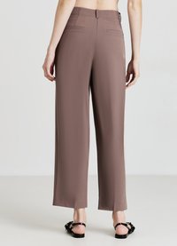 Hochgeschnittene, weite Hosen aus mauvefarbenem Stoff. Verfügt über minimalistische Gesäßtaschen und eine glatte Textur. Kombiniert mit schwarzen Sandalen.