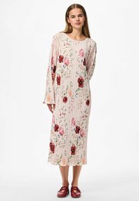 Cvjetna midi haljina svijetlo roza boje s nabranim dizajnom, na kojoj se nalaze crvene i ljubičaste cvjetove. Dugački rukavi i mekani materijal, u kombinaciji s crvenim obućom.
