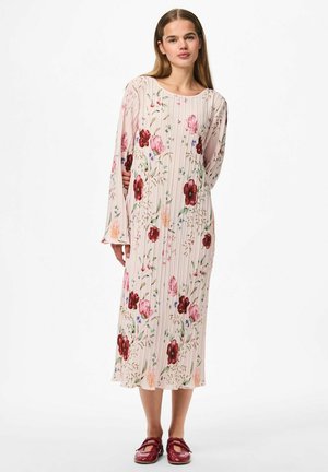 Vestido midi floral en rosa claro con un diseño plisado, con flores rojas y moradas. Mangas largas y textura suave, combinado con calzado rojo.