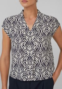 Blouse à manches courtes en bleu marine et crème avec un motif de feuilles, décolleté en V et texture de tissu douce. Coupe ajustée avec un ourlet droit.