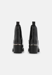 Černé kotníkové boty z lakované kůže s blokovým podpatkem, elastickými bočními panely a zlatým akcentem kolem paty, s texturovanou podrážkou.