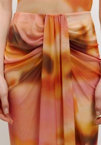 Dieser Rock besteht aus einem leichten, fließenden Stoff mit einem Farbverlauf in Orange, Pink und Braun, der an der Taille gerafft ist, um Textur zu erzeugen.