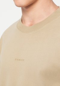 Μπεζ φούτερ από μαλακό βαμβάκι, με ριμπ λαιμόκοψη και μικρό κεντημένο λογότυπο σε ταιριαστό χρώμα στο στήθος.