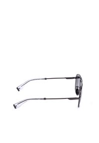 Lunettes de soleil fines à monture métallique avec des verres foncés et des embouts en plastique transparent sur les branches fines posées à plat sur une surface blanche.