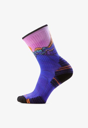 Calcetín vibrante con parte superior rosa, cuerpo púrpura, patrón abstracto de paisaje en azul y naranja, secciones de punta y talón negras con acentos naranjas.
